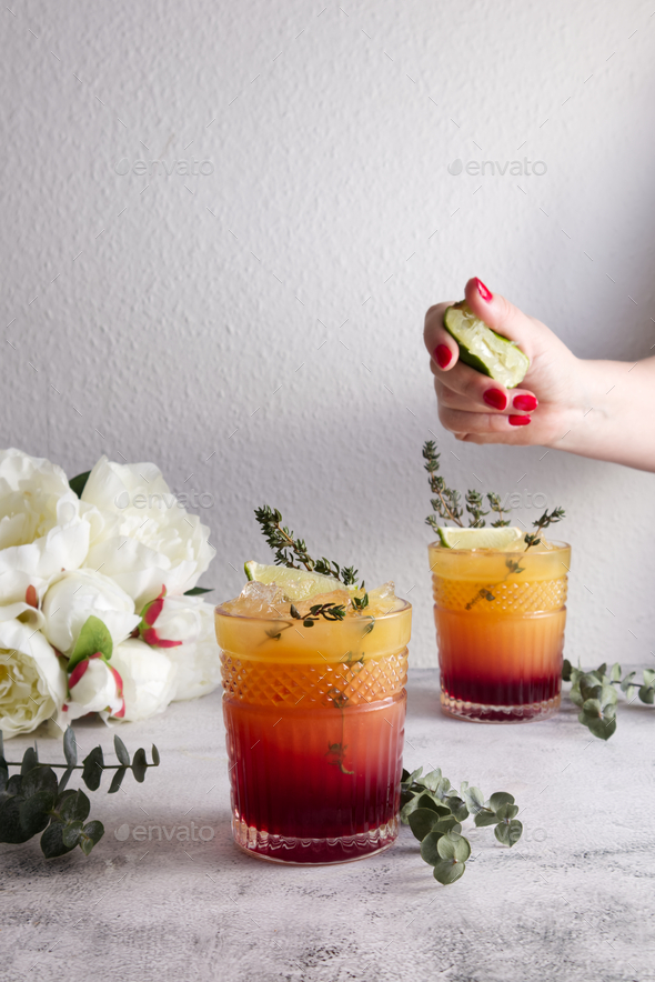 A woman\'s hand squeezes a lime over a glass with a fresh cocktail of orange and grenadine syrup