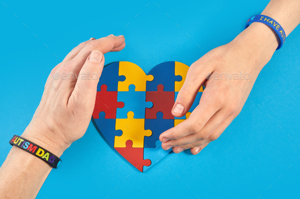 Father and autistic son hands holding jigsaw puzzle heart shape. World Autism Awareness Day