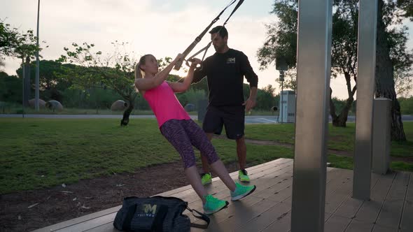 Training of a Blonde Woman with a Personal Fitness Trainer in the Park on Straps to Improve Her