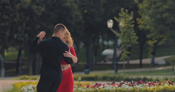 Elegant Man Dancing with a Beautiful Woman in a Red Tango Dress in a City Park