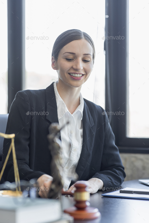 Statue of Justice and female lawyer in suit at workplace with laptop