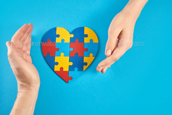 Father and autistic son hands holding jigsaw puzzle heart shape. World Autism Awareness Day