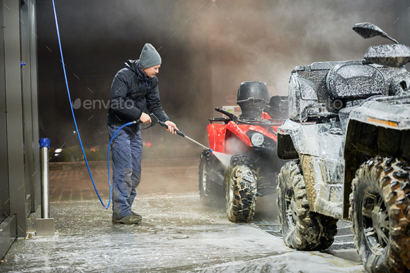 Man washing all-terrain vehicle with high pressure washer.