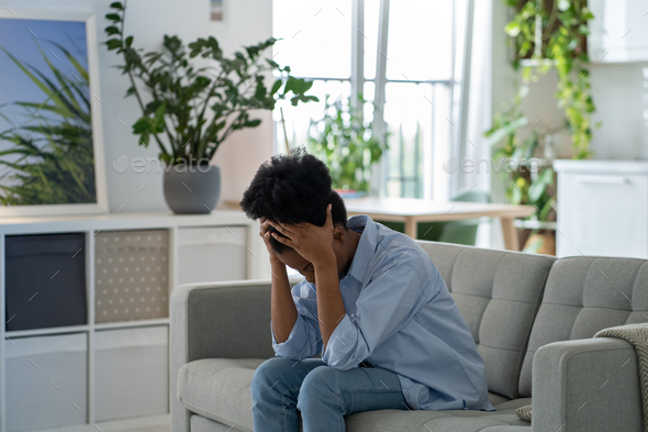 Depressed exhausted unhappy young woman sits on home couch hiding face ...