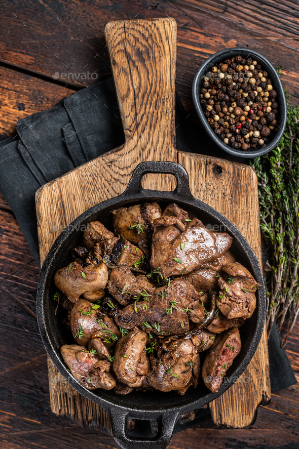 Roasted chicken liver with onions in a skillet. Wooden background. Top