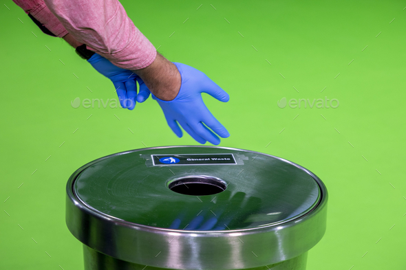 Hands remove glove on green background and dump into trash can.