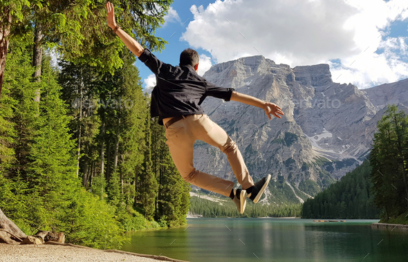 Shallow focus of a person jumping and heel kicking near a lake surrounded by rocky hills