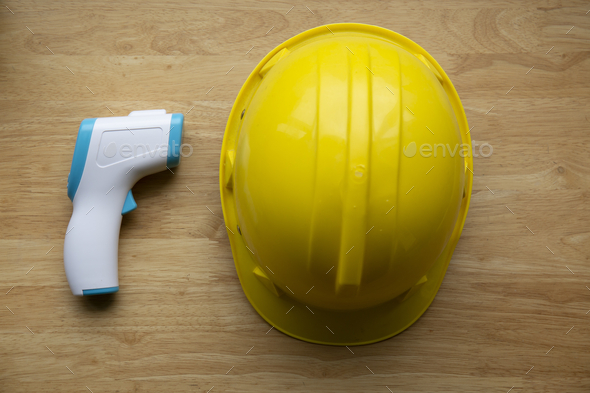 Top view of a medical thermometer and a yellow hard hat on a wooden t