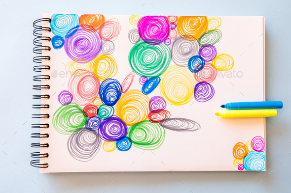 Closeup shot of colorful spiral drawings in a notepad on a blue surface