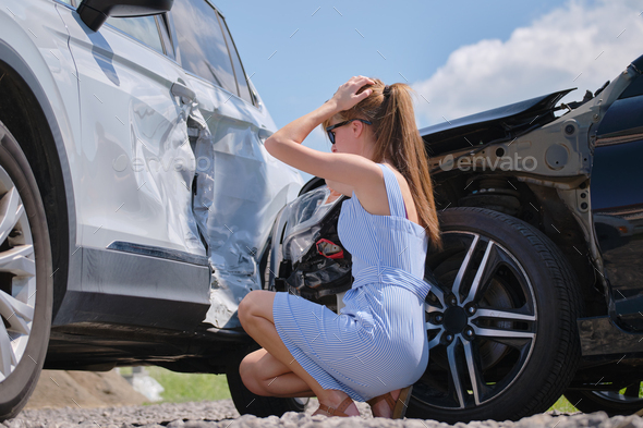 Sad female driver sitting on street side shocked after car accident. Road safety and vehicle