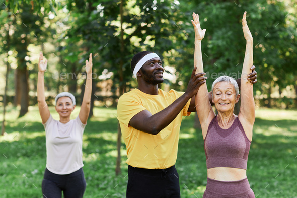 Smiling sports trainer assisting active senior woman in outdoor workout