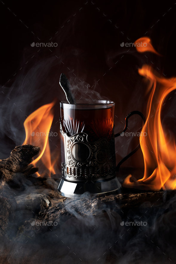 Glass tea in cup holder, playing tongues, flame reflections, smoke on background wooden driftwood