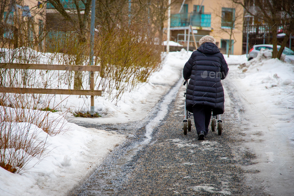 Elderly woman walking with a walker down the snow-covered street