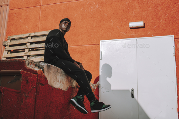 Athletic Black man sitting on a building ledge