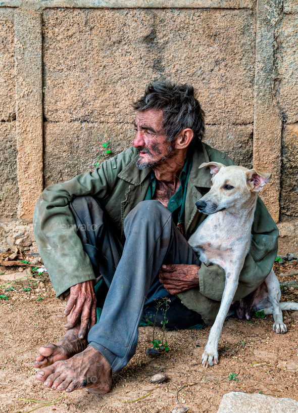Vertical shot of a black homeless man sitting outdoors with a dog - Stock Photo - Images