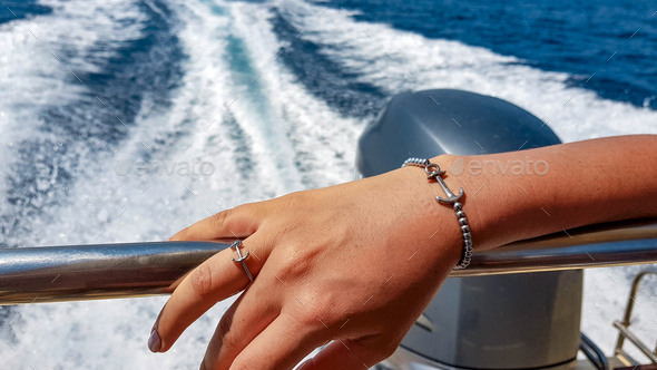 Closeup shot of a woman hand wearing an anchor ring and bracelet on boat metal railings