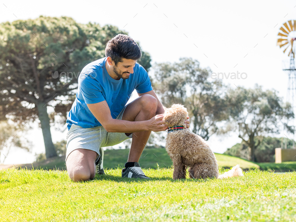 Young Caucasian male playing with his Goldendoodle dog on a professional golf course