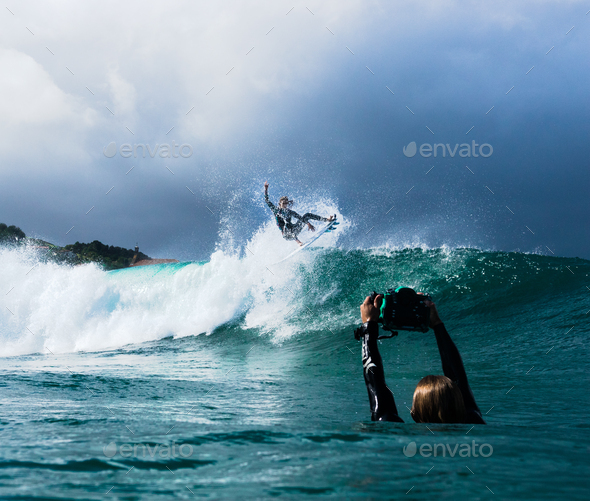 Surfer taking a picutre of his friend surfing the foamy wave of the ocean Stock Photo by wirestock
