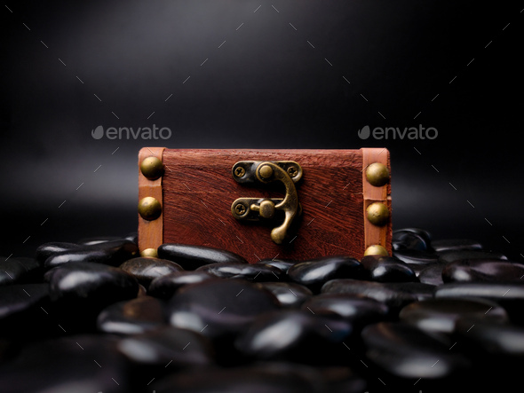 A locked mysterious wooden chest surrounded by black stones is on a black background. - Stock Photo - Images