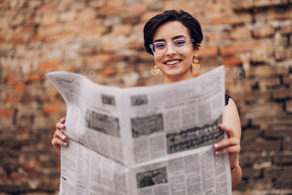 Portrait of a woman with eyeglasses reading newspaper outside