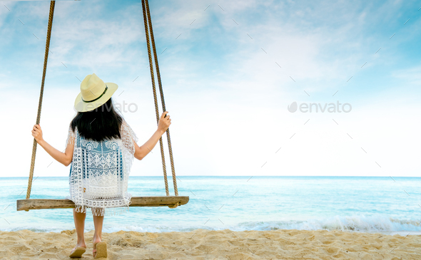 Asian woman in casual style wear hat and sandals sit on swings at sand beach  and looking sea - Stock Photo - Images