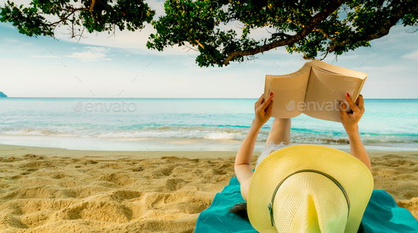 Woman lie down on green towel that put on sand beach under the tree and reading a book. Slow life - Stock Photo - Images