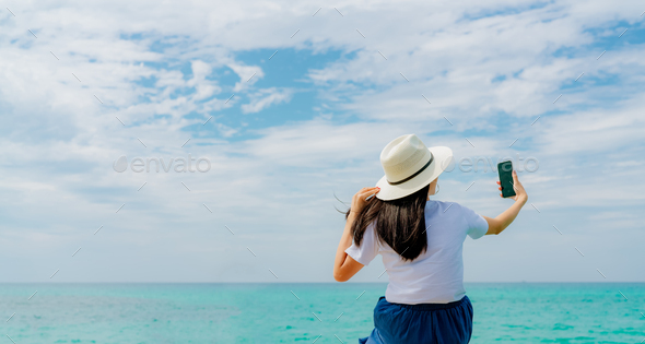 Young Asian woman wear straw hat use smartphone taking selfie at wooden pier. Summer vacation - Stock Photo - Images