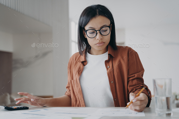 Woman in glasses counting expenses on calculator manages family budget at home. Financial management