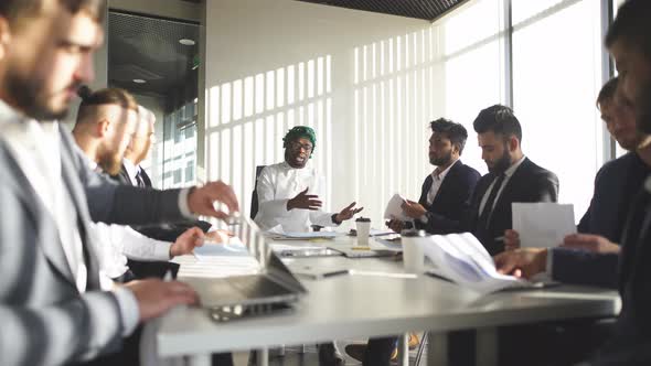Multiracial Male Business Executives Discuss Project Sitting at Conference Table alt