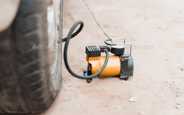 Inflating air into tire with car compressor outdoors. Close-up, selective focus on electric pump