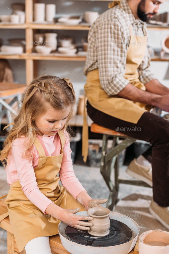 child making ceramic pot on pottery wheel with teacher in workshop