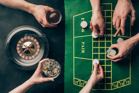 Hand with whiskey and chips by casino table with bets and roulette