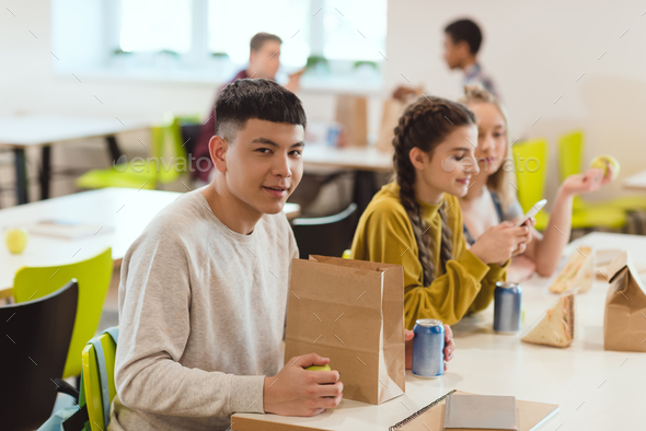 A group of cheerful small school kids in canteen, eating lunch and talking.  stock photo