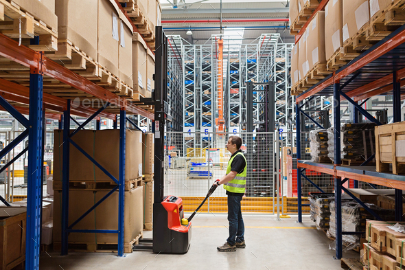 Storehouse employee in uniform working on forklift in modern automatic warehouse. Boxes are on the