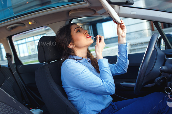 Business woman sitting in the car and apply make up.