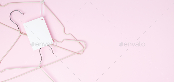 Creative flat lay hangers with white paper label pink background. Clothing tag, label blank mockup t