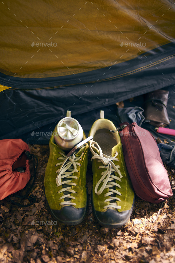 Closeup shot of hiking boots, first aid kit, Thermo mug, and camp for camping