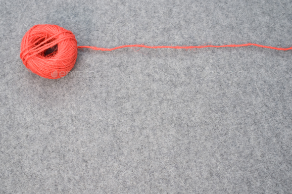 Ball of red yarn with a loose string stretching to the side on a gray  background with copy space Stock Photo by wirestock