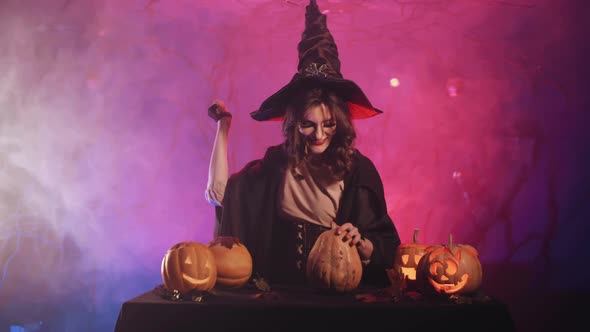 A beautiful witch conjures and laughs as she cuts out a pumpkin for halloween. Halloween! 4K.