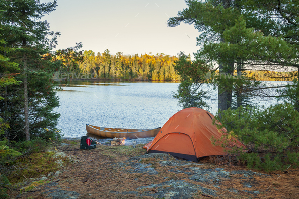Campsite with orange tent and canoe on northern Minnesota lake at sunrise during autumn - Stock Photo - Images