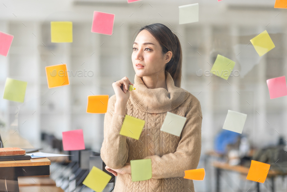 Business Asian woman meeting at office and use post it notes in glass wall to share idea. Brainstorm