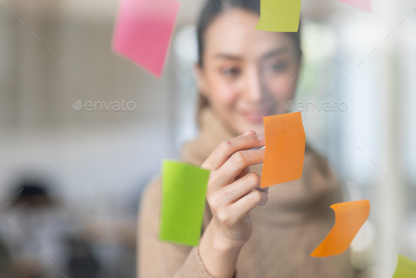 Business Asian woman meeting at office and use post it notes in glass wall to share idea. Brainstorm