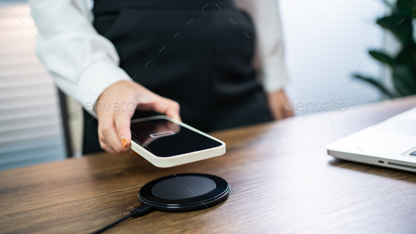 Charging mobile phone battery with wireless charging device in the table.