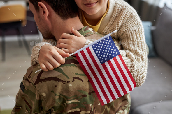 Close up of girl embracing military dad and holding american flag
