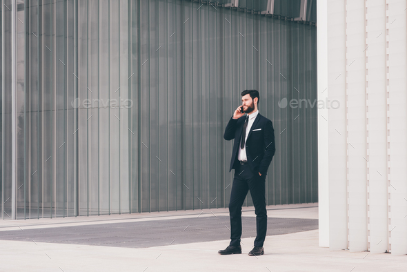 Young bearded elegant businessman outdoors using smartphone talking - Stock Photo - Images
