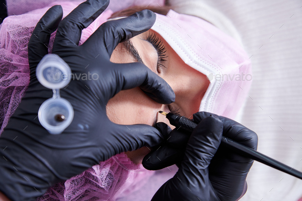 Beauty salon worker microblading the eyebrows of a client