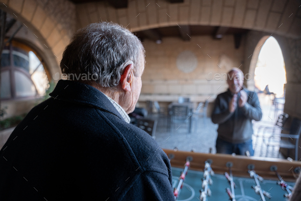 An old man is using a hearing aid while playing table football with his family