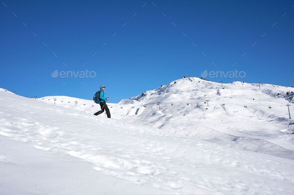 Female hiker with walking sticks on a snowy mountain under a clear cloudless sky