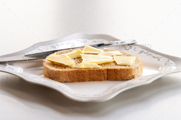 Closeup of a piece of toast with small pieces of butter on it served on a ceramic plate with a knife