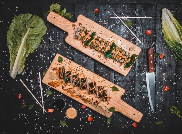 Two wooden plates with sushi placed on a table with knife and lettuce